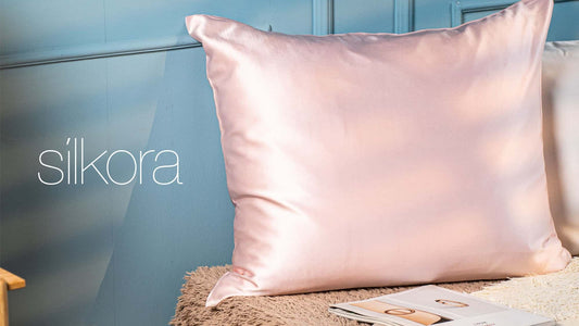 Zijden kussensloop van Silkora in Lotus Roze op een bed voor een blauwe wand