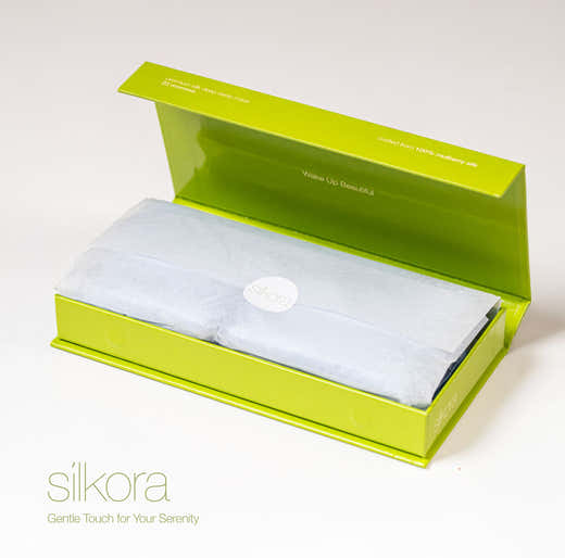 Geöffnete grüne Geschenkbox von Silkora mit der Schlafmaske in durchscheinendem Papier und einem runden Silkora-Aufkleber