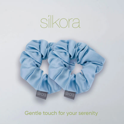 Twee grote Silkora scrunchies in icy blauw op een lichte achtergrond met het Silkora-logo en de tekst "Gentle touch for your serenity".