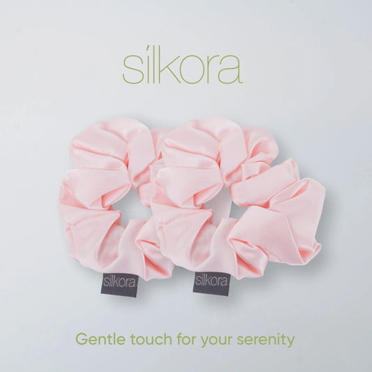 Twee grote Silkora scrunchies in lotus roze op een lichte achtergrond met het Silkora-logo en de tekst "Gentle touch for your serenity".