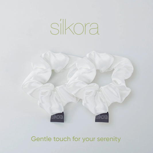 Twee grote Silkora scrunchies in wit op een lichte achtergrond met het Silkora-logo en de tekst "Gentle touch for your serenity".