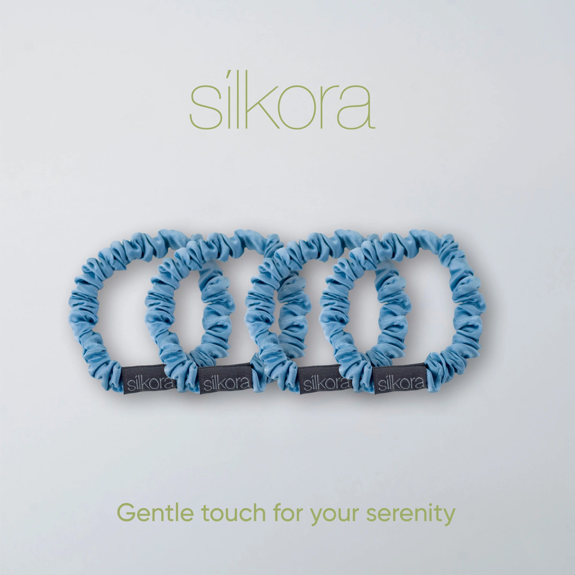 Vier kleine Silkora scrunchies in icy blauw op een lichte achtergrond met het Silkora-logo en de tekst "Gentle touch for your serenity".