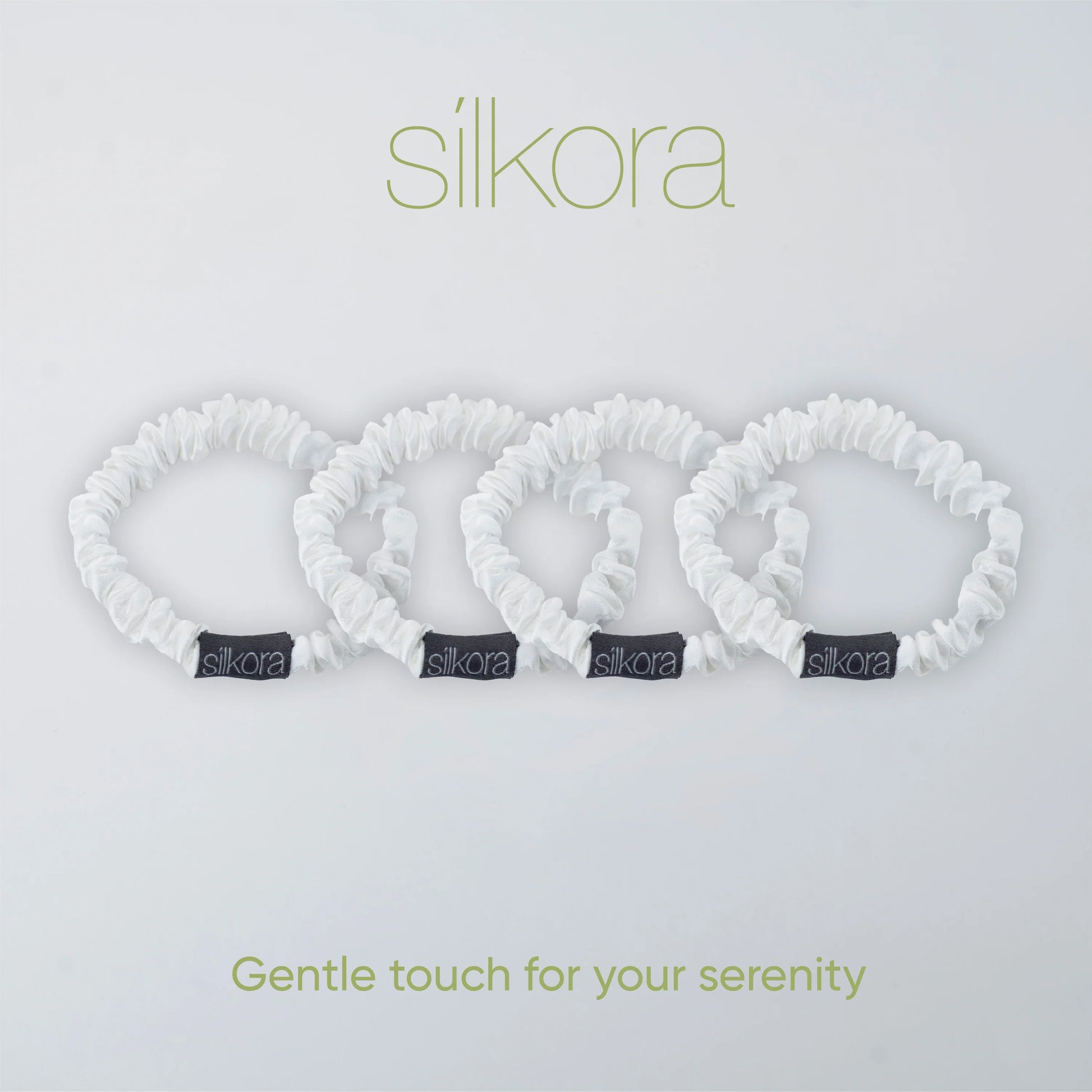 Vier kleine witte Silkora scrunchies op een lichte achtergrond met het Silkora-logo en de tekst "Gentle touch for your serenity".