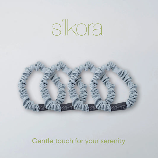 Vier kleine Silkora scrunchies in zilvergrijs op een lichte achtergrond met het Silkora-logo en de tekst "Gentle touch for your serenity".